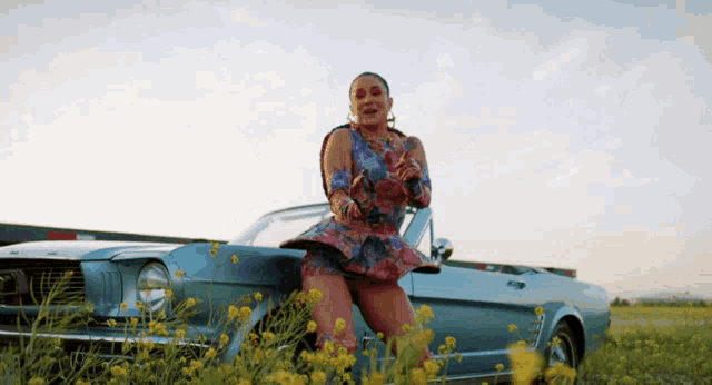 a woman in a colorful dress is standing next to a mustang in a field of yellow flowers .