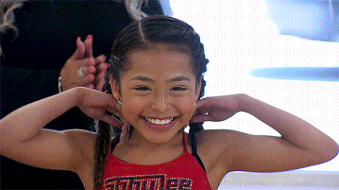 a young girl wearing a red tank top with the word muscles on it smiles