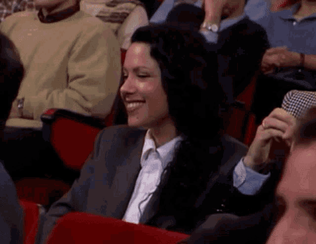 a woman in a suit is smiling while sitting in a theatre audience .