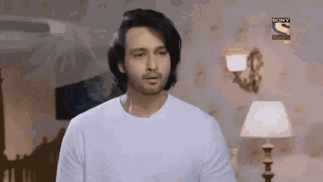 a man in a white shirt is standing in a room with a lamp and a sony logo on the wall