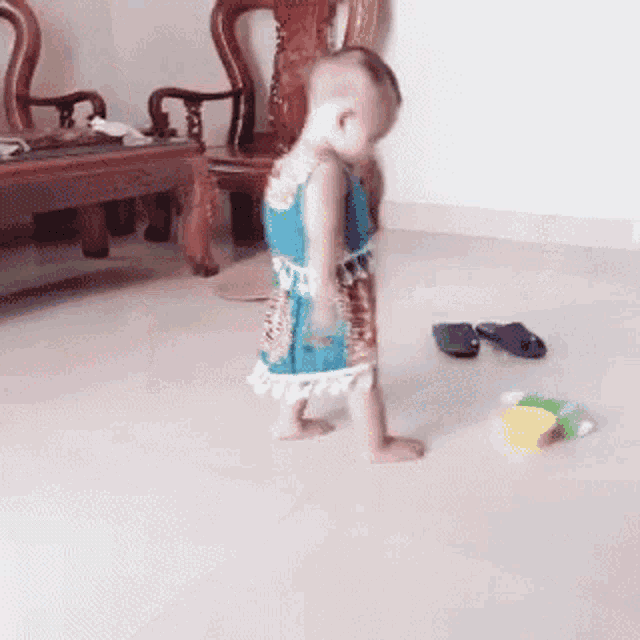 a baby is walking on the floor in a living room next to a table and chairs .