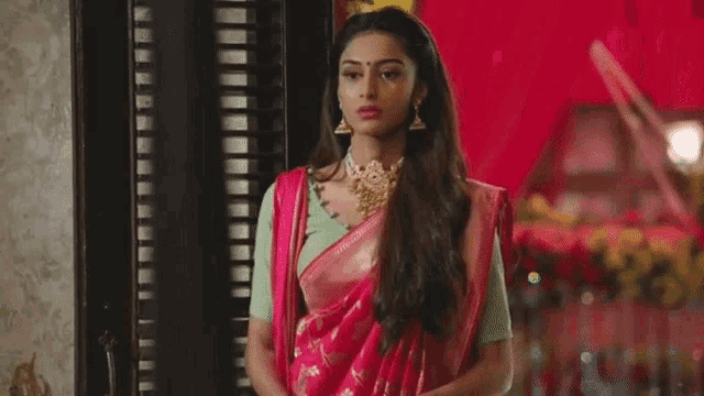 the woman is wearing a pink saree and a green blouse .