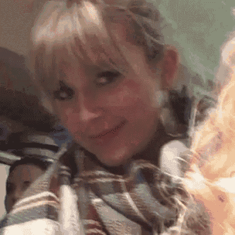 a close up of a woman 's face with blonde hair and a plaid scarf around her neck .