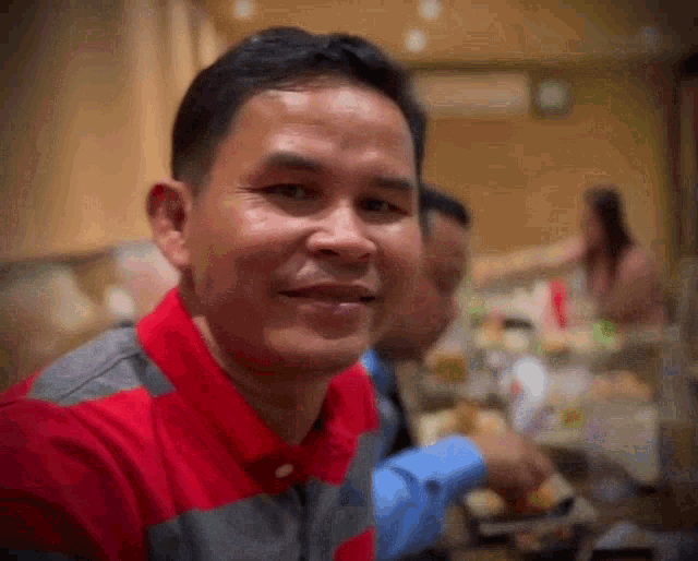 a man in a red and gray shirt is smiling at the camera