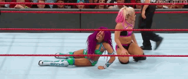 two women are wrestling in a wrestling ring and one is laying on the floor .