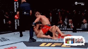 two men are wrestling in a ufc ring with an advertisement for 2 shots in every can behind them