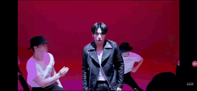 a man wearing a black leather jacket and a hat is dancing with two other men .