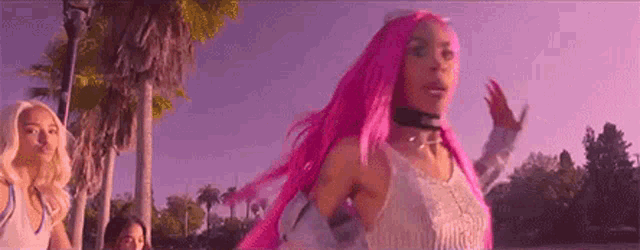 a woman with pink hair is standing in front of palm trees in a park .