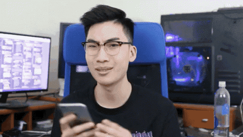 a man wearing glasses holds a cell phone in front of a computer monitor