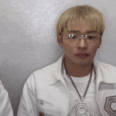 a man wearing glasses and a white jacket has a necklace with a pendant that says c on it