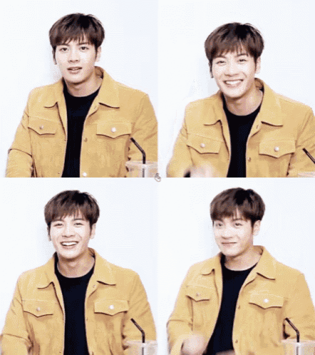 a young man wearing a yellow jacket is smiling and holding a drink