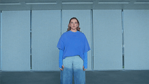 a woman in a blue shirt and jeans stands in a room