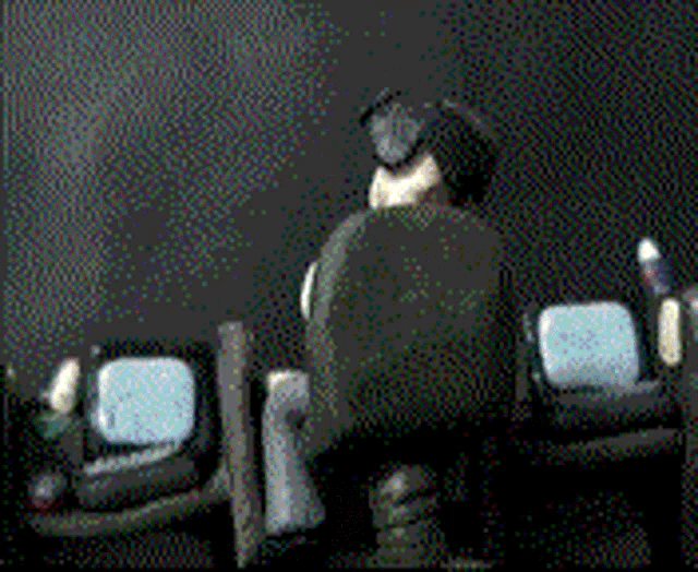 a man wearing headphones sits in a dark room watching a television
