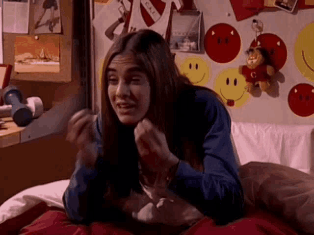 a woman is sitting on a bed with a smiley face wall behind her .