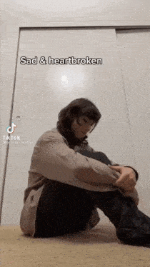 a woman is sitting on the floor with her legs crossed and a caption that says sad and heartbroken .