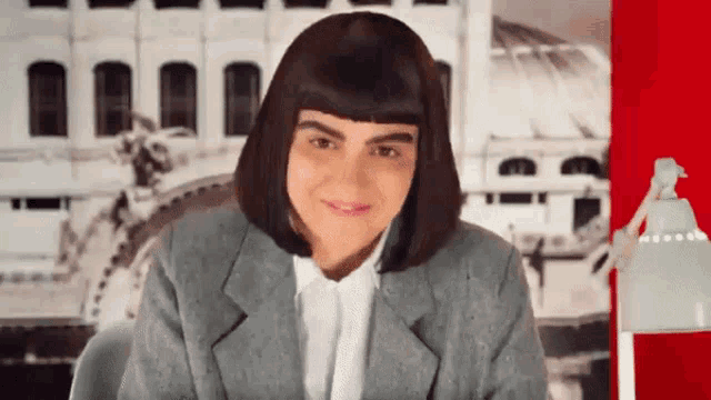 a woman wearing a wig and a suit is smiling in front of a building