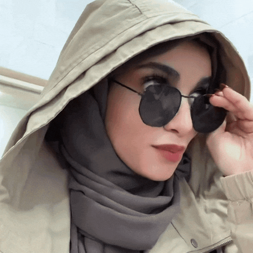 a woman wearing a hijab and sunglasses adjusts her glasses