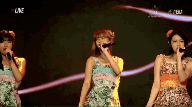 three women singing in front of a sign that says new era