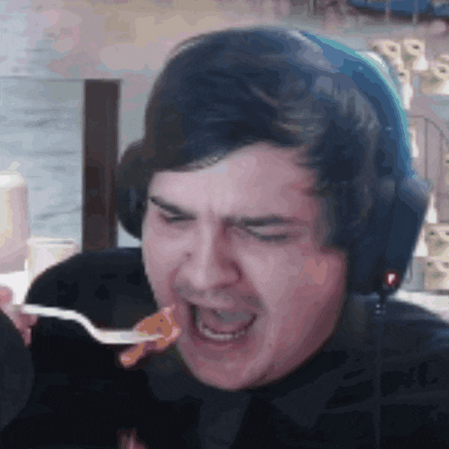 a man in headphones is eating a piece of food with a fork .