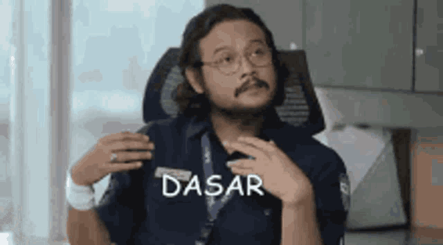 a man with a beard is sitting in a chair with the word dasar written on his chest