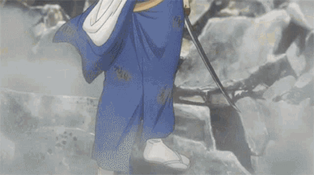 a man in a blue robe is holding a sword in his hand while standing on a rocky hillside .