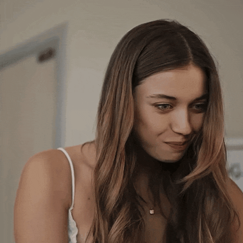 a woman with long hair wearing a white tank top and a necklace