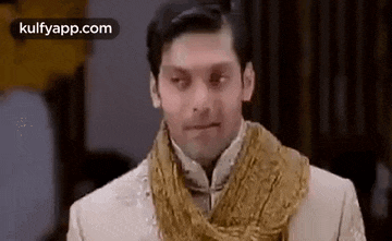 a man in a suit and scarf is making a funny face and looking at the camera .
