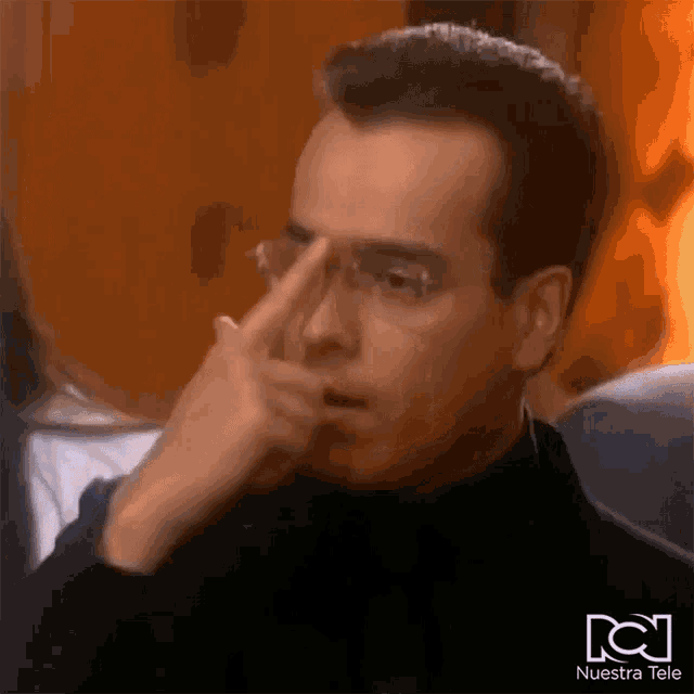 a man with glasses is pointing at his nose .