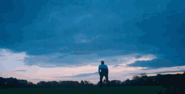 a man is standing in a field with a cloudy sky in the background