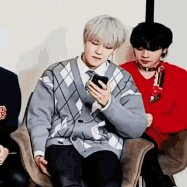 a man in a sweater is sitting in a chair looking at his phone .