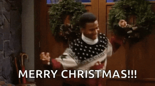 a man in a sweater is dancing in front of a door and says `` merry christmas ! ''