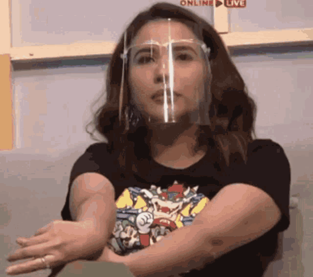 a woman wearing a face shield and a black t-shirt is sitting at a table .