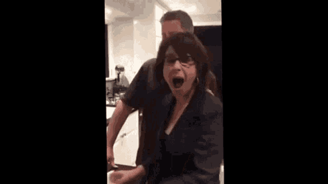 a man in a suit is standing in a kitchen with a woman standing behind him .