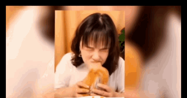 a woman is eating a sandwich and making a face .