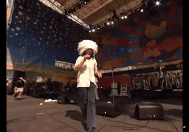 a man singing into a microphone while wearing a white feathered hat
