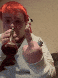a man with red hair is smoking a pipe and giving the middle finger