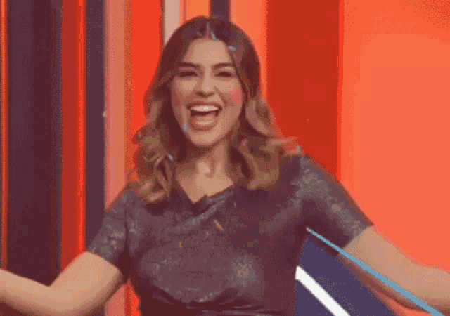 a woman is laughing with her mouth open and her arms outstretched in front of a red wall .