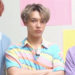 a young man in a colorful shirt is standing with his arms crossed in a room .