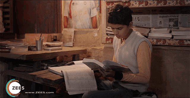 a boy sits at a table reading a book with a zee5 logo on the bottom right