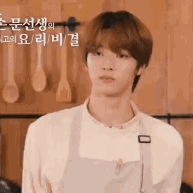 a young man wearing a white apron is standing in front of a wooden wall .