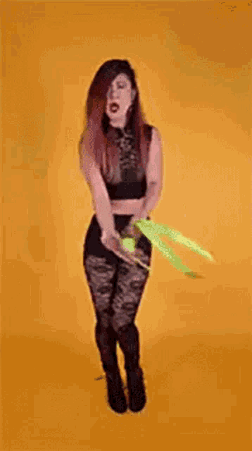 a woman in a crop top and high waisted pants is standing in front of a yellow background .