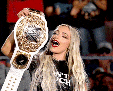 a woman wearing a black shirt that says ' n't touch ' on it is holding a championship belt