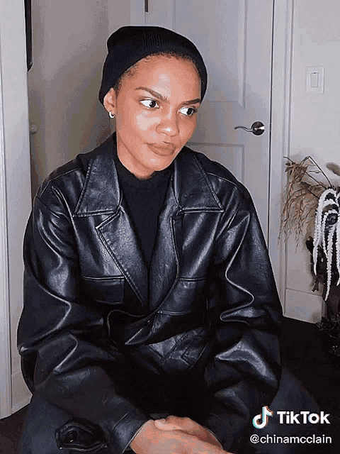 a woman wearing a black leather jacket and a black beanie has a tiktok sticker on her face