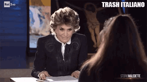 a woman is sitting at a table talking to another woman with trash italiano written on the screen