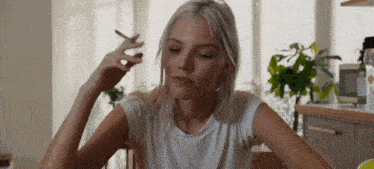 a young woman is smoking a cigarette while sitting at a table .