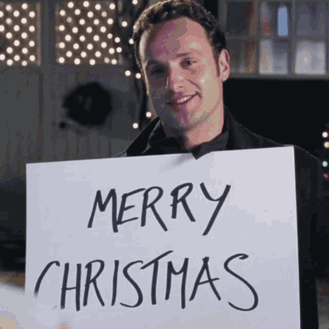 a man holding up a sign that says merry christmas