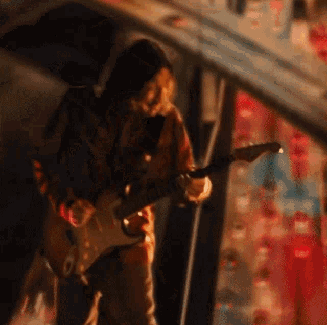 a man in a red jacket is playing an electric guitar