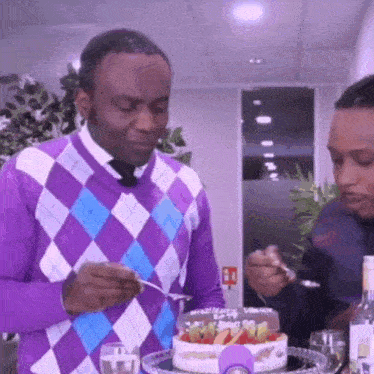 a man in a purple and blue plaid sweater is eating a birthday cake