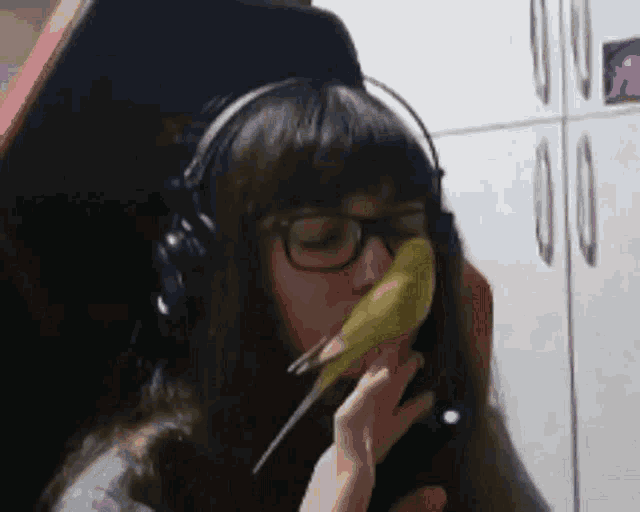 a girl wearing headphones holds a small bird in her mouth