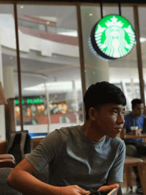 a young man sits at a table in front of a starbucks sign